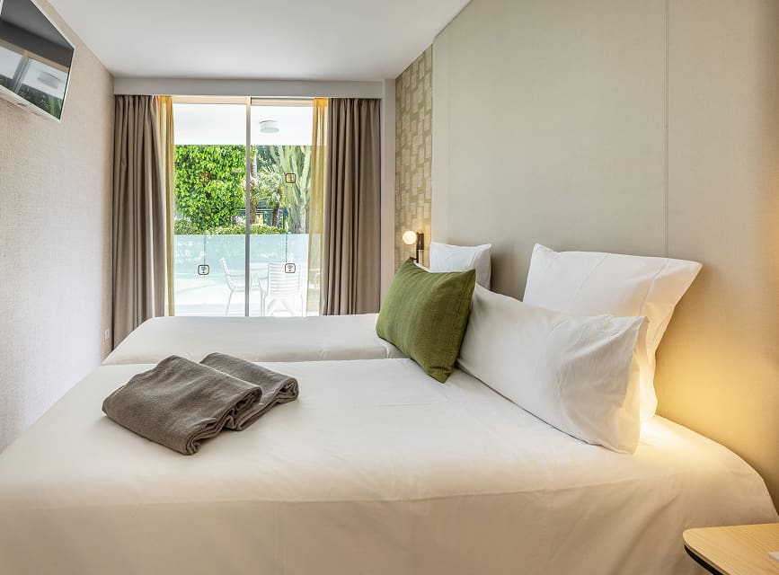 Apartment bedroom in Puerto Pollensa Bedroom with two single beds pushed together, green cushion and large window overlooking the Illa d'Or Apartments garden