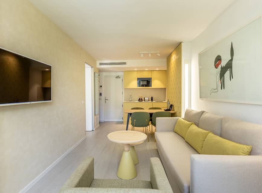 Apartment living room with sofa and TV Living room with sofa, armchair and TV, with the kitchen and dining area behind, in a Puerto Pollensa apartment