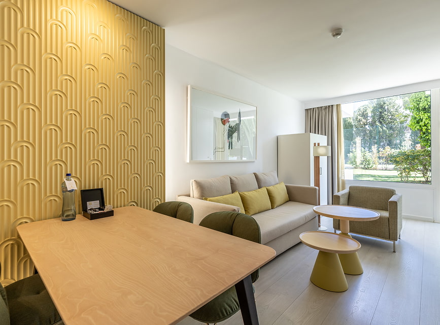 Holiday apartment in Puerto Pollensa Living and dining area with table, sofa and armchair beside a large window overlooking the garden in a bright apartment