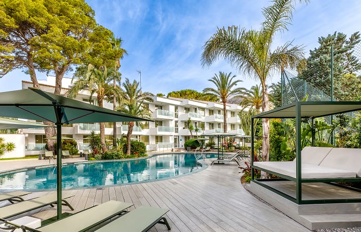 Apartments in Puerto Pollensa with pool Pool with Balinese beds and loungers among palm trees, in front of the Illa d'Or Apartments buildings