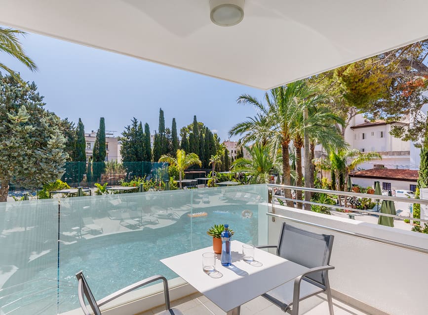 Studio terrace overlooking the pool Studio terrace with table, chairs and glass balustrade facing the pool and palm-filled garden