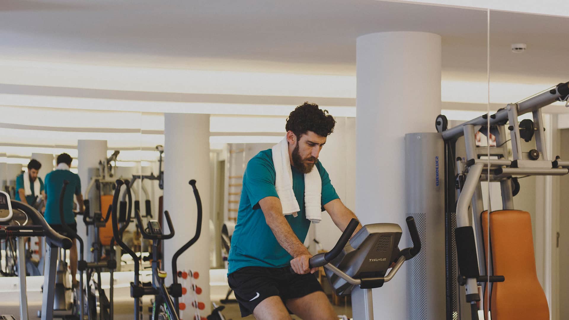 Mann trainiert auf einem Heimtrainer im Fitnessraum neben Kraftgeräten