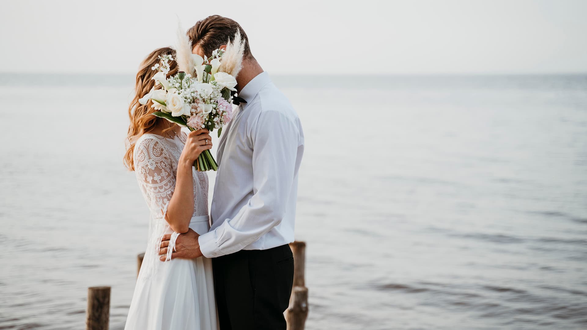Brautpaar umarmt sich mit dem Brautstrauß am Meer bei einer Hochzeit in Puerto Pollensa
