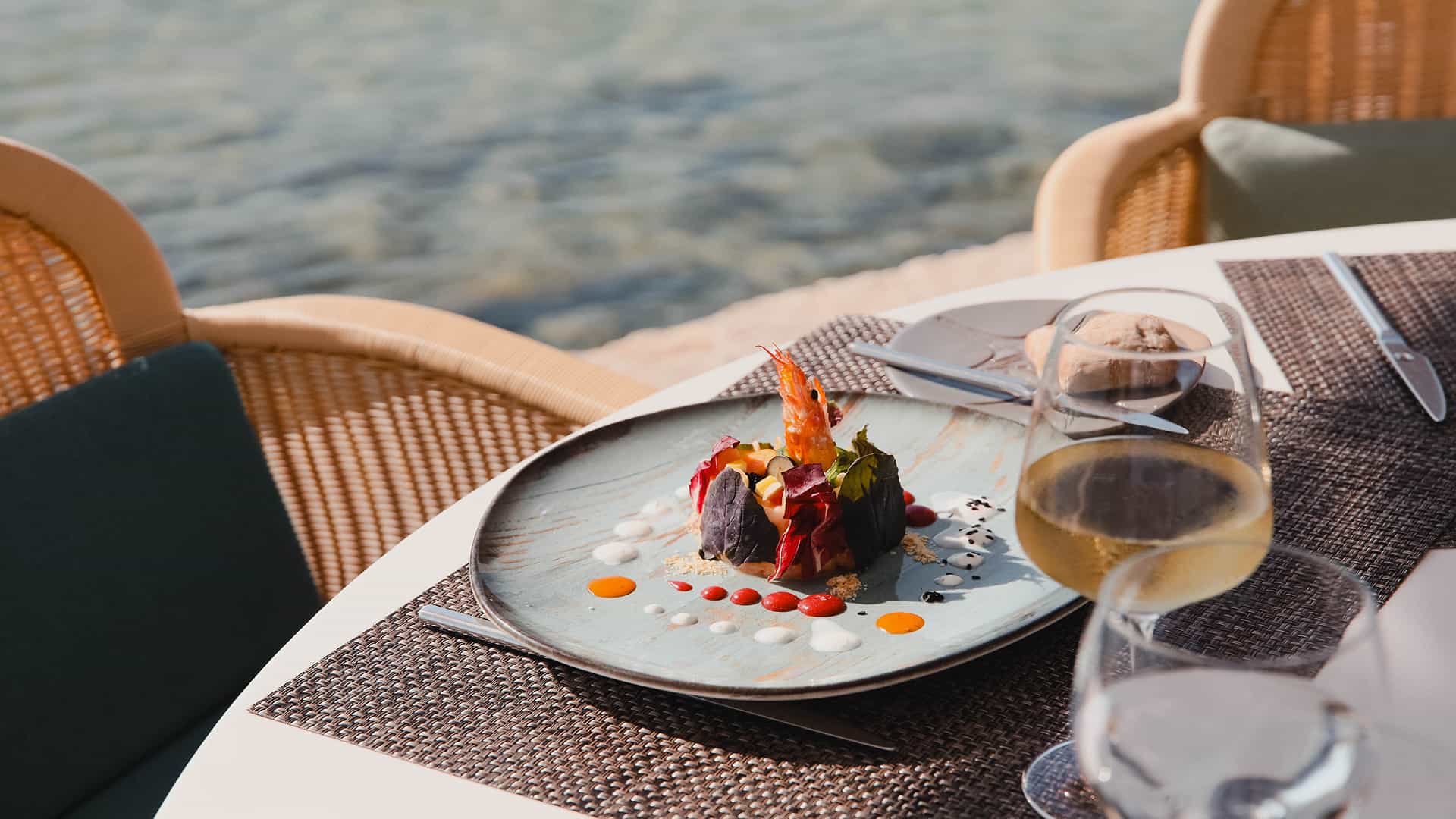 Hotel Illa d'Or restaurant by the sea Signature dish with prawn and a glass of white wine on a seaside table at the Hotel Illa d'Or restaurant