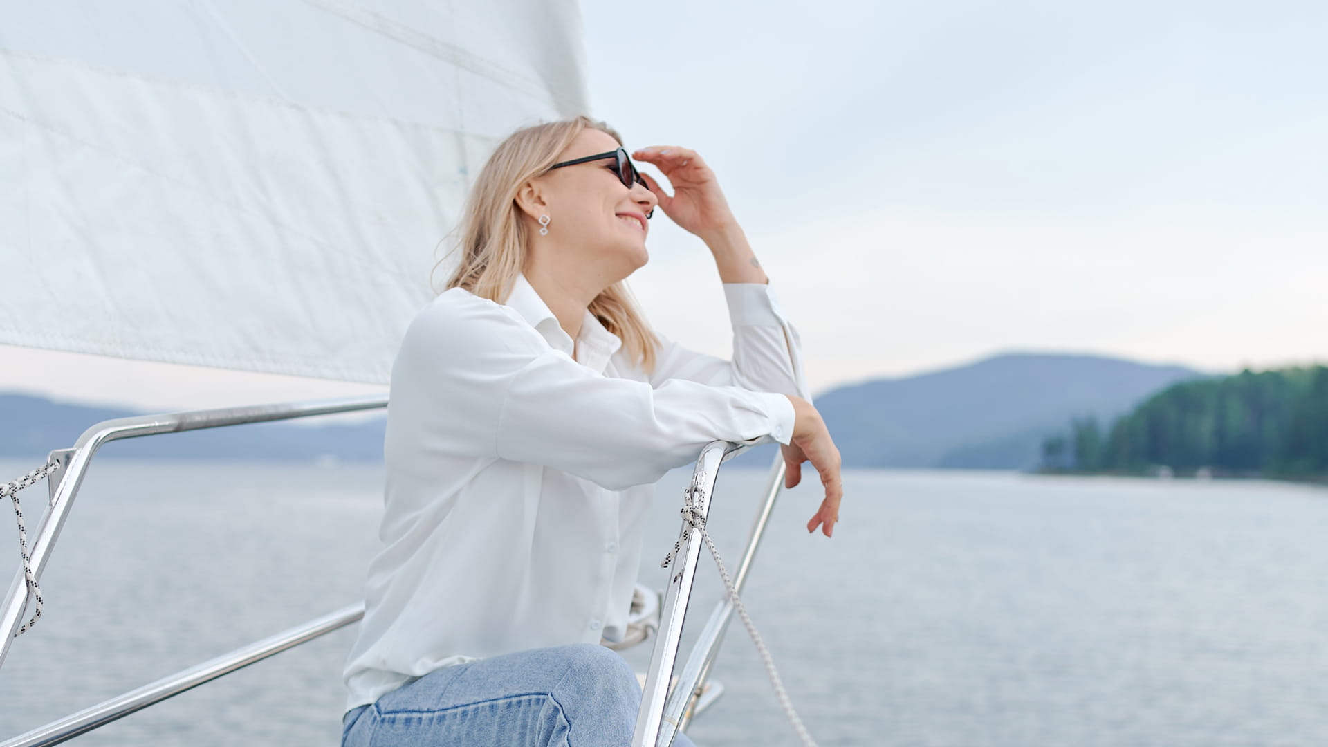 Woman sitting on the deck of a sailing boat enjoying the sun and views of the sea and coastline