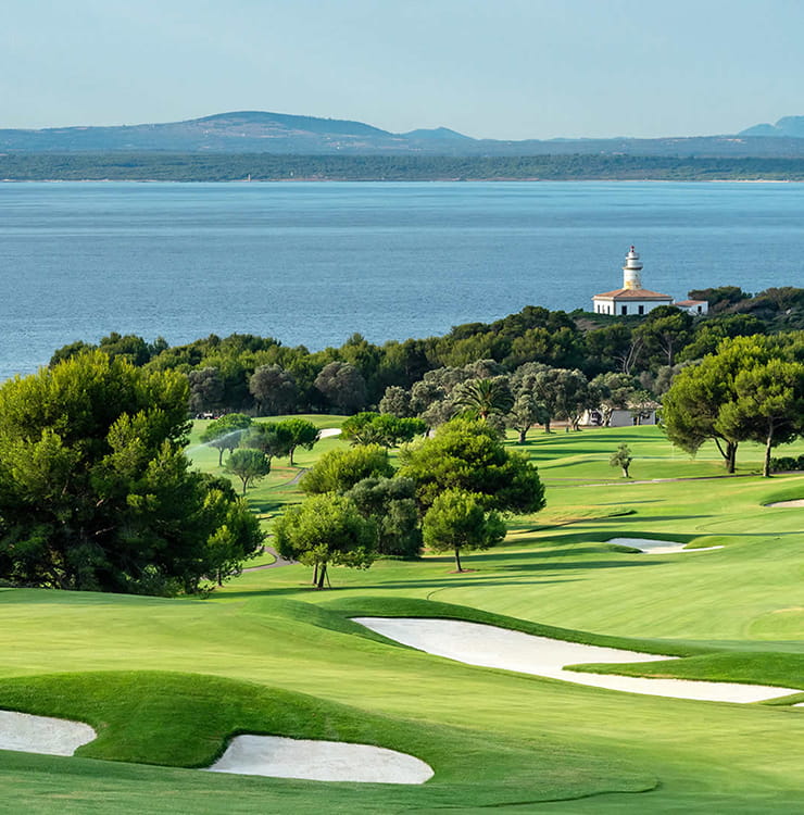 Golfplatz mit Meerblick, umgeben von Pinien, im Hintergrund ein Leuchtturm an der Küste