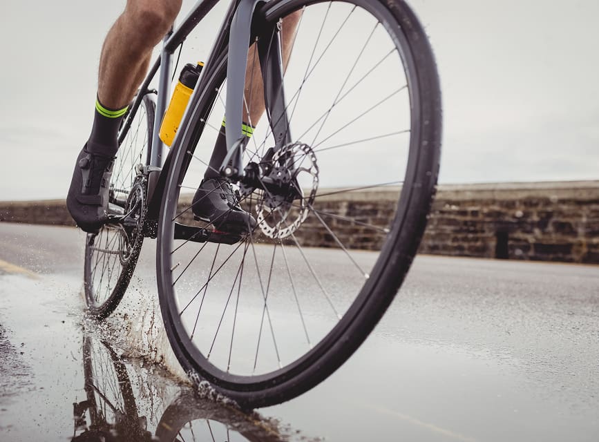Nahaufnahme eines Rennrads auf nassem Asphalt neben einer Steinmauer
