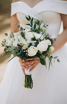 Braut im weißen Kleid mit einem Strauß aus weißen Rosen und Grün