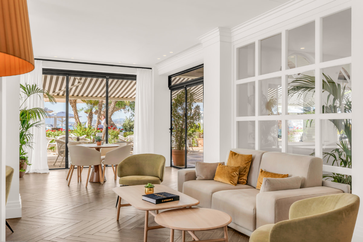 Helle Lounge mit Sofa, Sesseln und Couchtischen an großen Fenstern zur Terrasse und zum Garten
