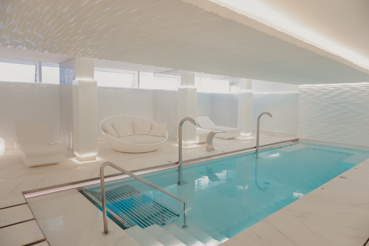 Innenpool im Spa mit Wasserdüsen, Einstiegstreppe und weißen Liegen