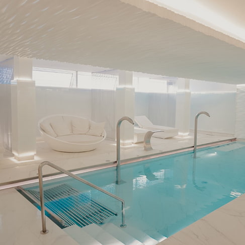 Innenpool im Spa mit Wasserdüsen, Einstiegstreppe und weißen Liegen