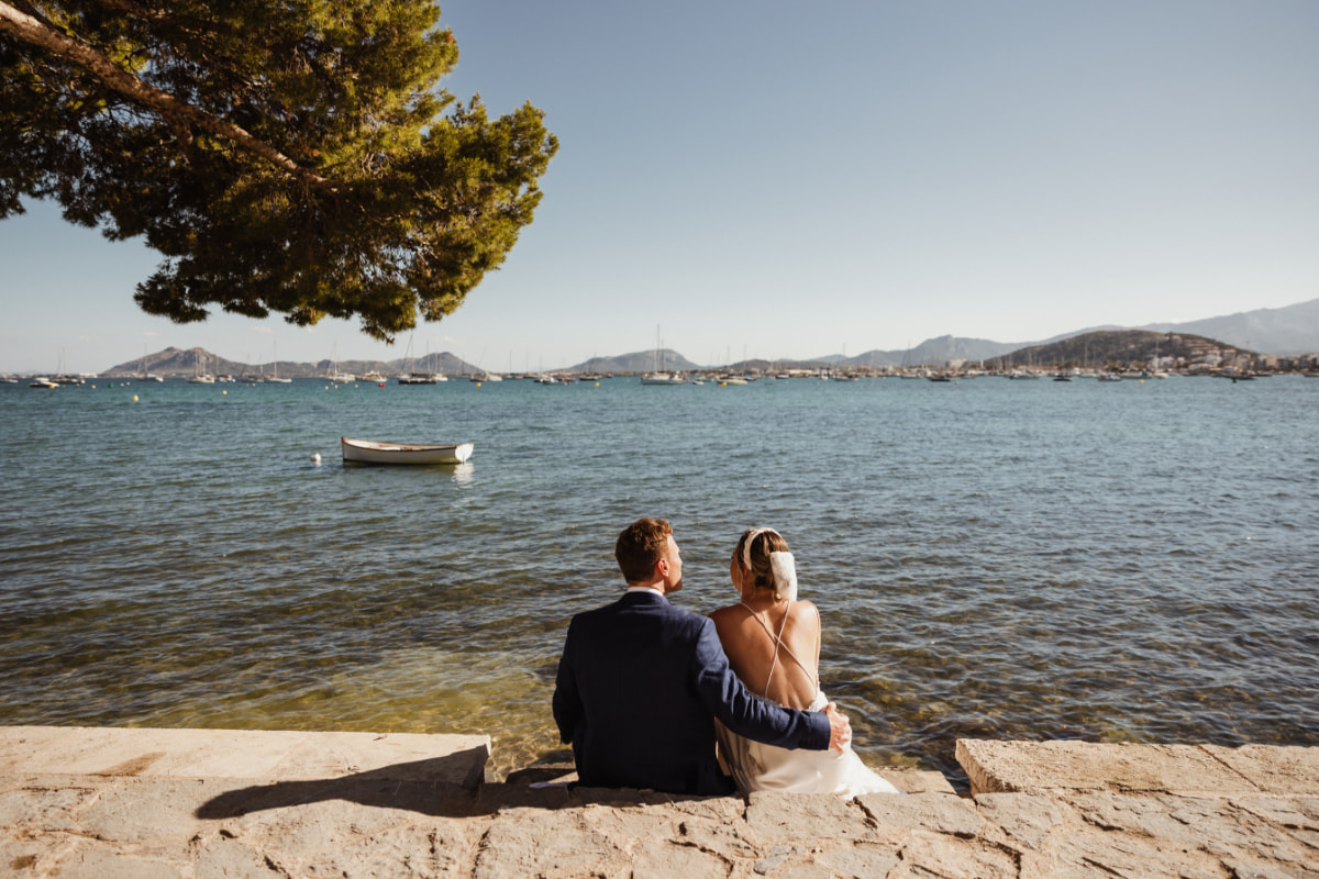 Brautpaar sitzt am Meer unter einer Pinie und blickt auf die Bucht von Pollença