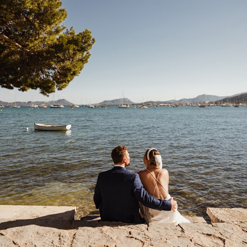 Brautpaar sitzt am Meer unter einer Pinie und blickt auf die Bucht von Pollença