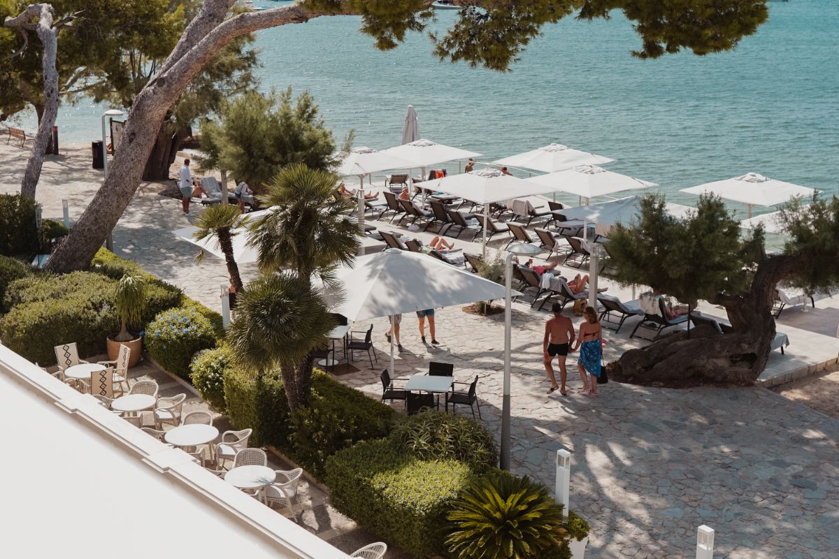 Hotelgarten mit Tischen an der Strandpromenade und Liegen mit Sonnenschirmen am Meer