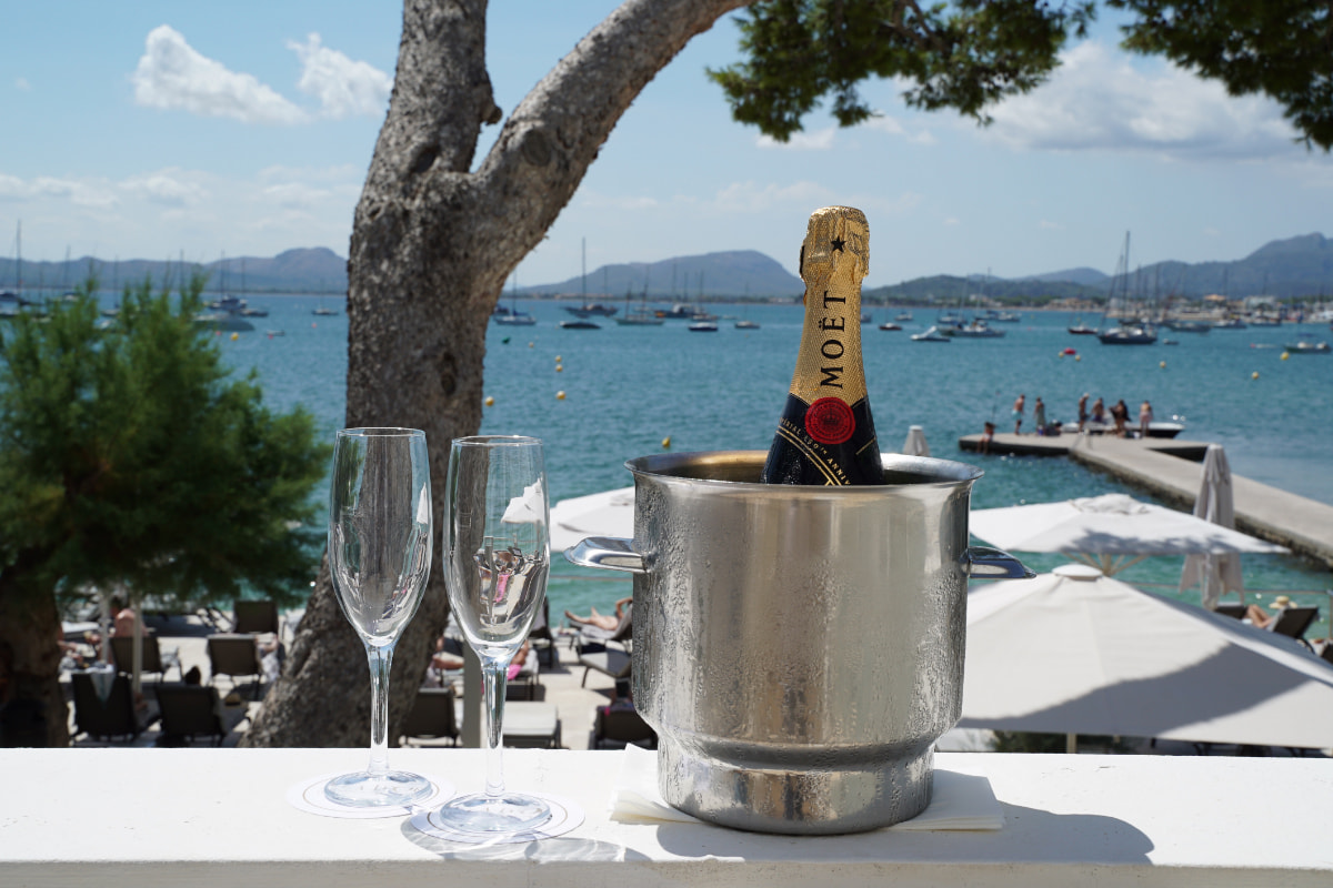 Champagnerflasche im Kühler und zwei Gläser auf einer Brüstung mit Blick auf Hafen und Bucht