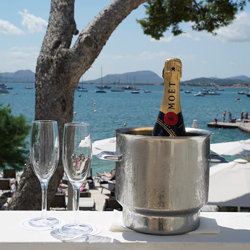 Champagnerflasche im Kühler und zwei Gläser auf einer Brüstung mit Blick auf Hafen und Bucht