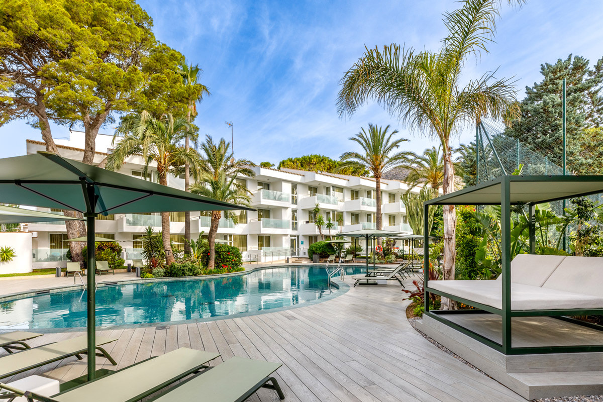Außenpool mit Balibetten, Liegen und Palmen neben dem Hotelgebäude in Puerto Pollensa