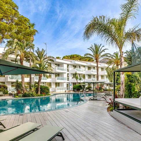 Außenpool mit Balibetten, Liegen und Palmen neben dem Hotelgebäude in Puerto Pollensa