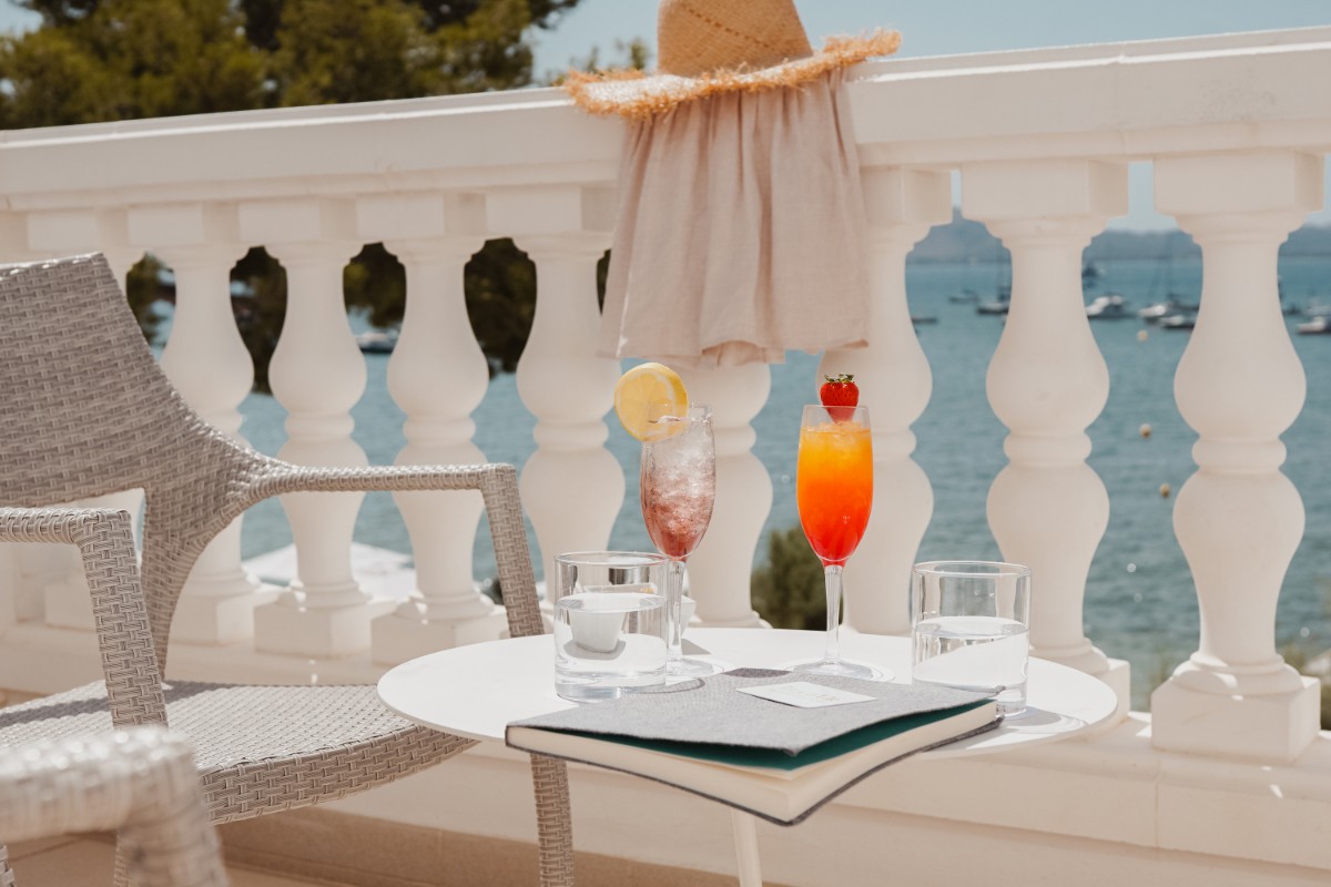 Zwei Cocktails und eine Karte auf einem Tisch auf der Terrasse mit weißer Balustrade und Blick auf die Bucht
