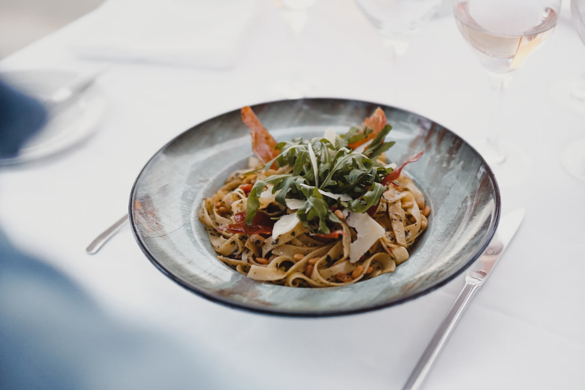 Teller Tagliatelle mit Gemüse, Parmesanspänen und frischen Kräutern auf weißer Tischdecke