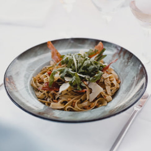 Teller Tagliatelle mit Gemüse, Parmesanspänen und frischen Kräutern auf weißer Tischdecke