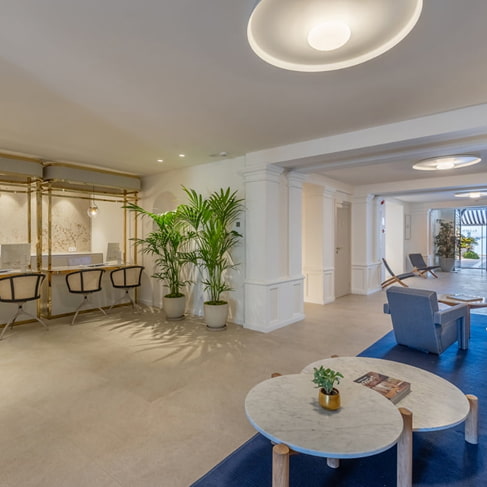 Großzügige Lobby mit Arbeitsbereich und Hockern, blauen Sesseln, Marmortischen und Pflanzen
