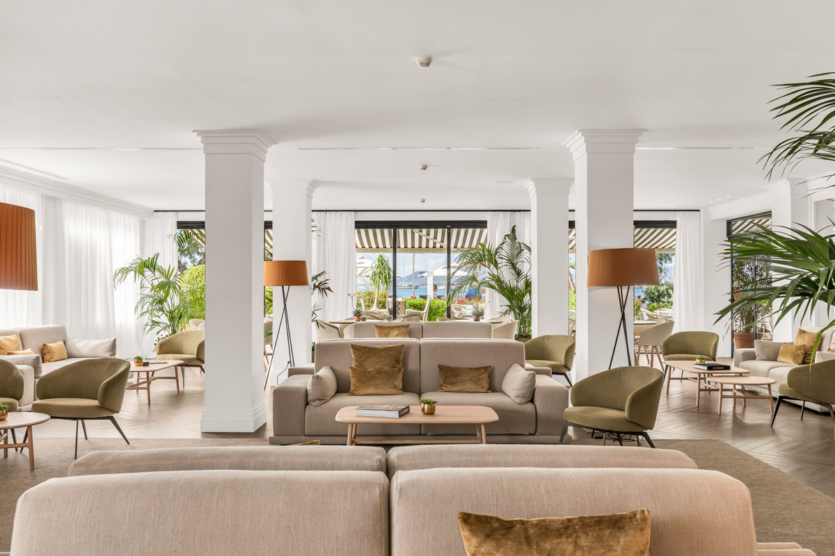 Großzügige Lounge mit Sofas, Sesseln, Stehlampen und weißen Säulen, durch große Fenster erhellt
