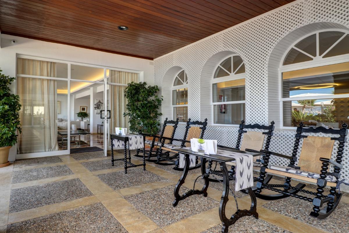 Überdachte Veranda mit Schaukelstühlen im mallorquinischen Stil, weißen Gitterbögen und Zugang zum Hotel