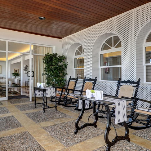 Überdachte Veranda mit Schaukelstühlen im mallorquinischen Stil, weißen Gitterbögen und Zugang zum Hotel