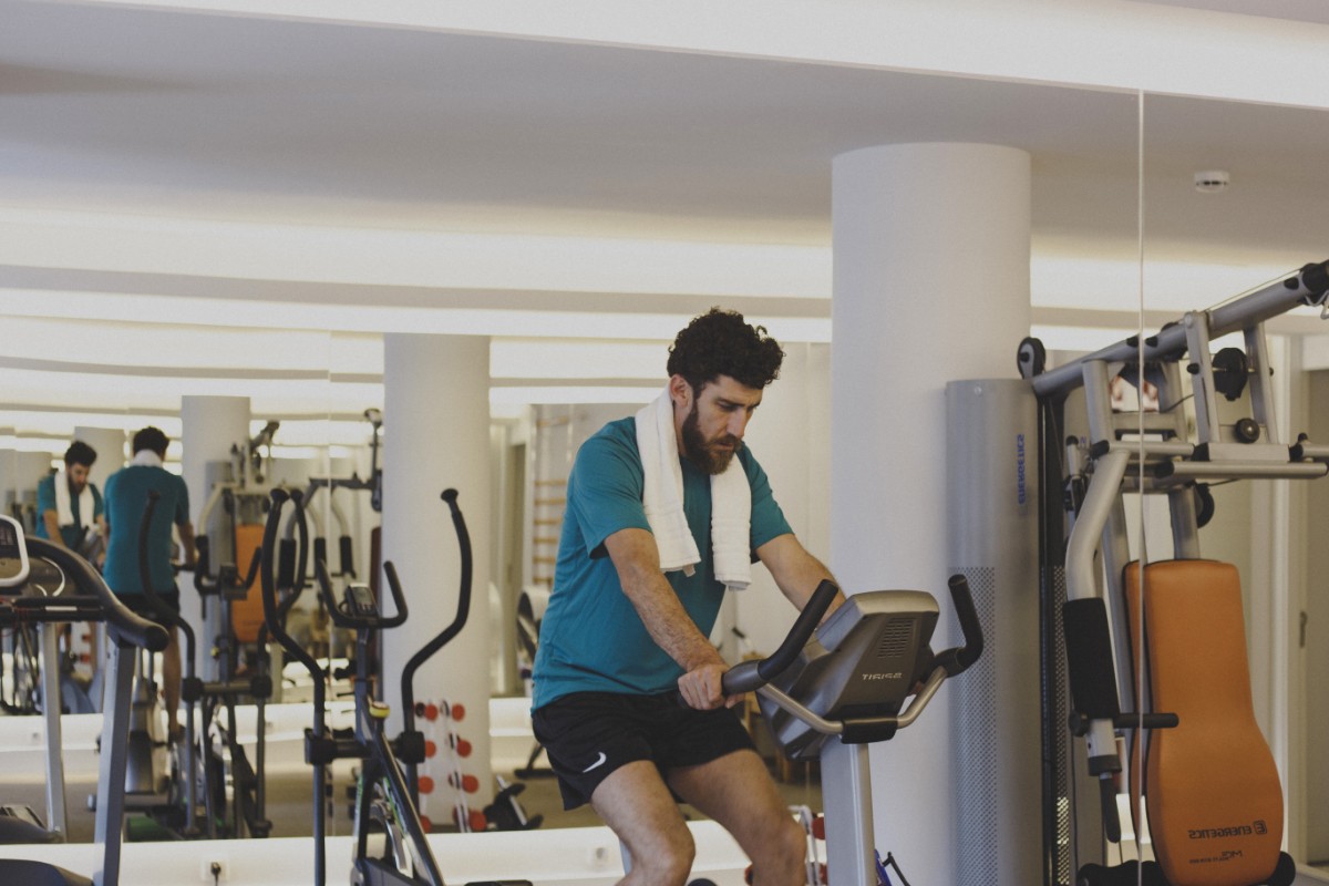 Mann auf einem Heimtrainer im Fitnessraum neben Kraftgeräten