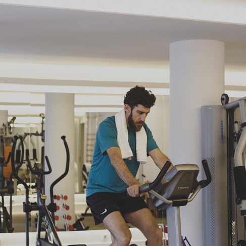 Mann auf einem Heimtrainer im Fitnessraum neben Kraftgeräten