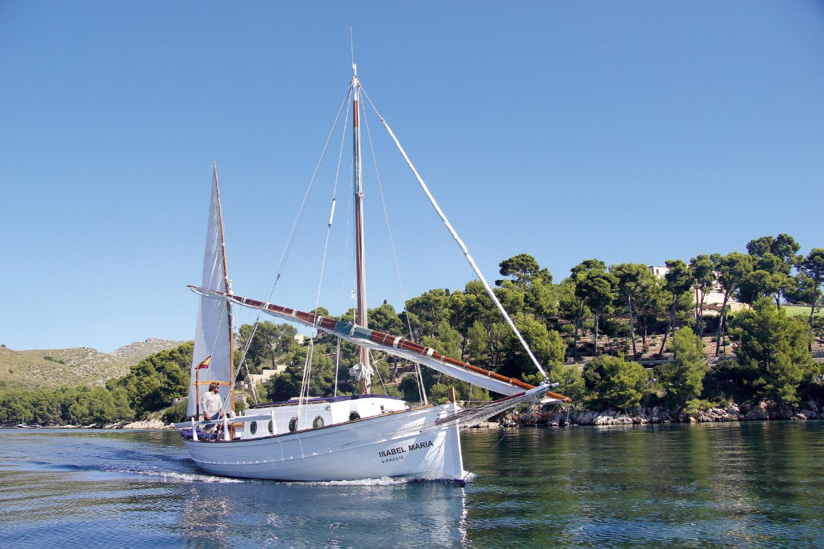 Traditionelles mallorquinisches Llaüt-Segelboot entlang der Küste, im Hintergrund Pinienwälder