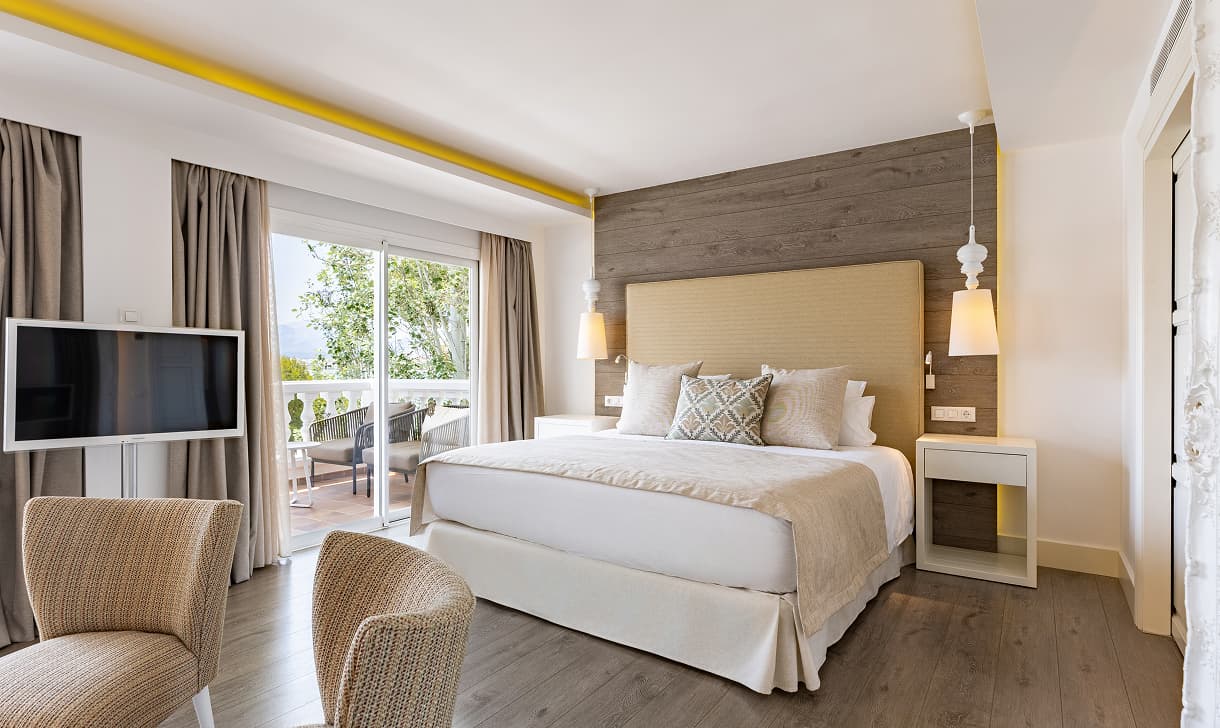 Doppelzimmer mit Doppelbett, Sesseln, Fernseher und Zugang zur privaten Terrasse mit Blick auf den Hotelgarten