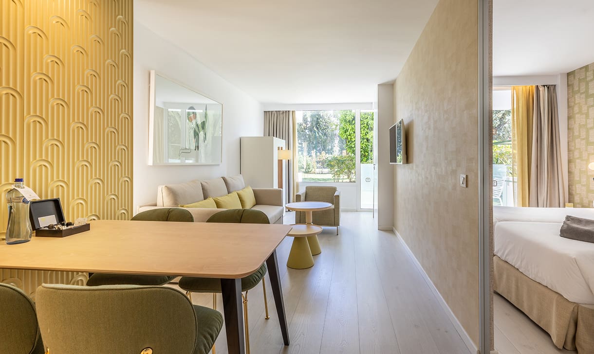 Heller Wohnraum mit Esstisch, Sofa und Sitzbereich, rechts das angrenzende Schlafzimmer