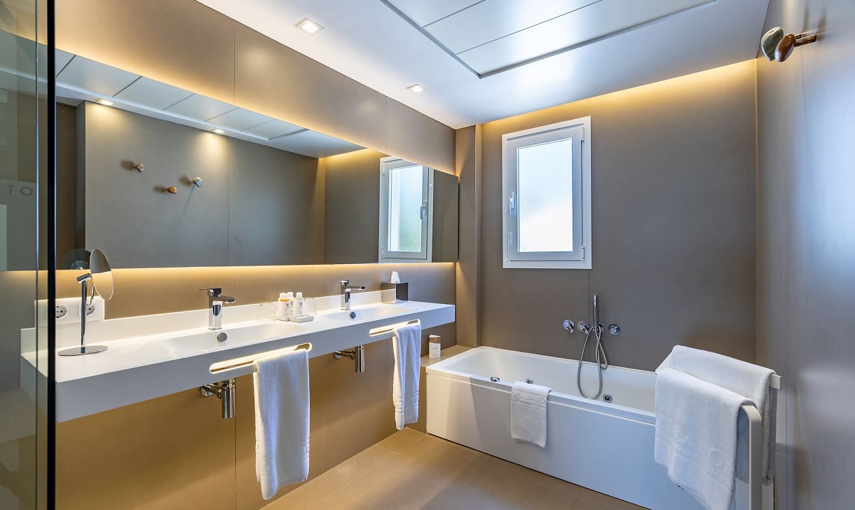 Modernes Badezimmer mit Badewanne, Doppelwaschbecken, beleuchtetem Spiegel und weißen Handtüchern