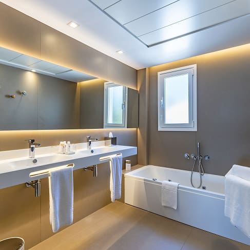 Modernes Badezimmer mit Badewanne, Doppelwaschbecken, beleuchtetem Spiegel und weißen Handtüchern