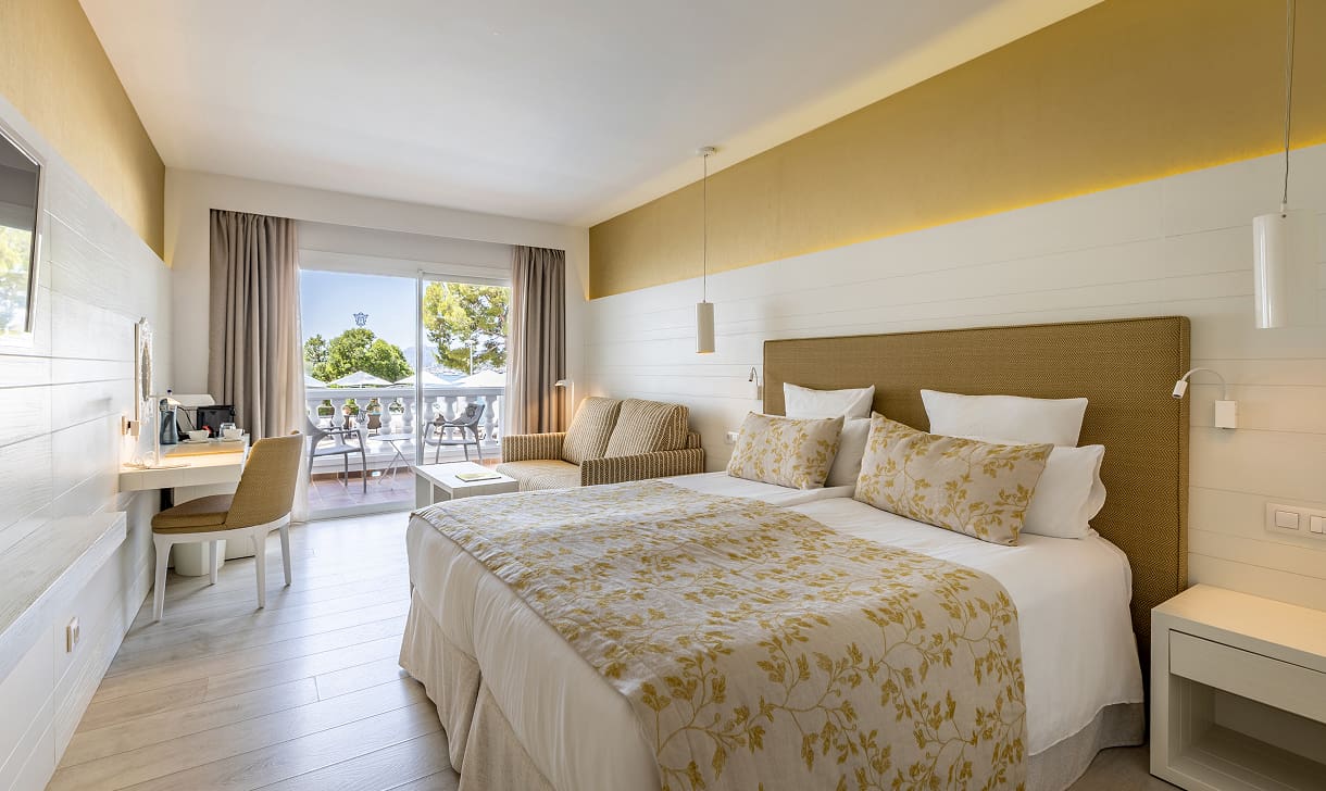 Zimmer mit zusammengestellten Betten, goldfarbener Blumen-Tagesdecke, Arbeitsbereich und Terrasse zum Garten