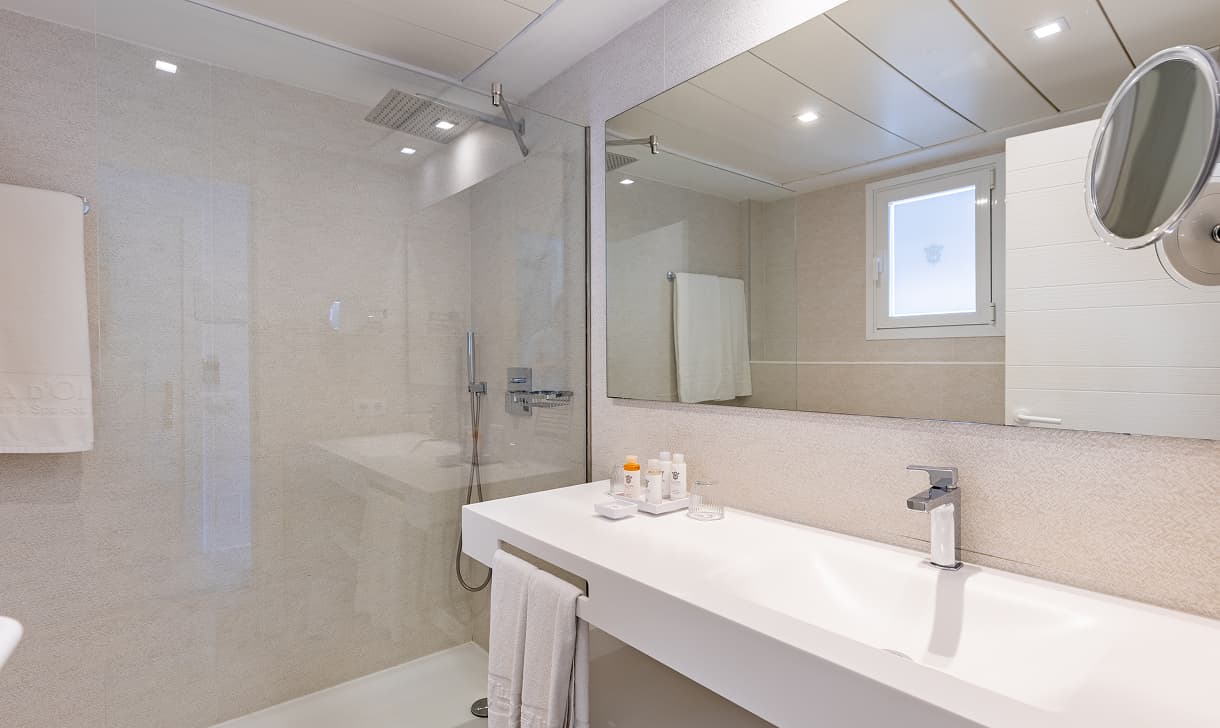 Badezimmer mit verglaster Regendusche, großem Waschbecken, Kosmetikspiegel und Pflegeprodukten
