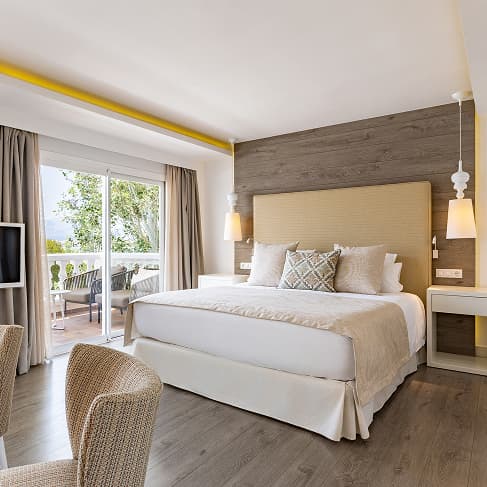 Doppelzimmer mit Doppelbett, Sesseln, Fernseher und Zugang zur privaten Terrasse mit Blick auf den Hotelgarten