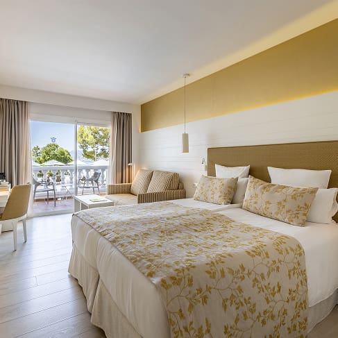 Zimmer mit zusammengestellten Einzelbetten, geblümter Tagesdecke, Schreibtisch, Sofa und Terrasse in Puerto Pollensa