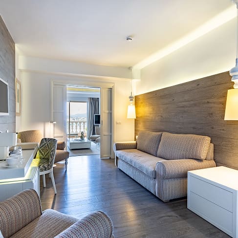 Wohnbereich mit Sofa, holzverkleideter Wand, Minibar und Kaffeemaschine, im Hintergrund der Blick nach draußen