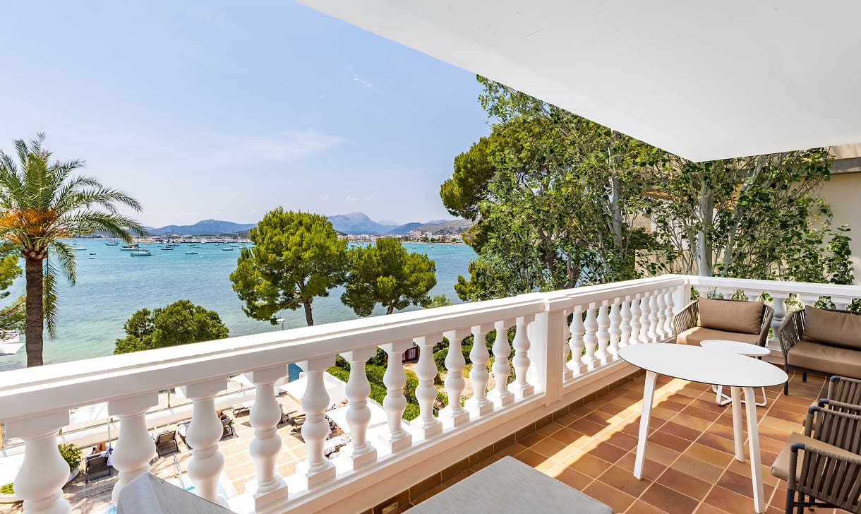 Private Terrasse mit Tisch und Stühlen, weißer Balustrade und Blick auf die Bucht zwischen Palmen und Pinien
