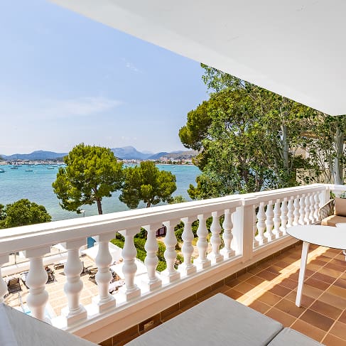 Private Terrasse mit Tisch und Stühlen, weißer Balustrade und Blick auf die Bucht zwischen Palmen und Pinien
