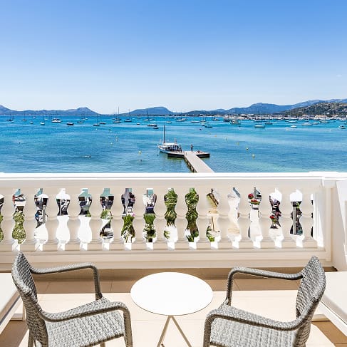 Balkon mit zwei Stühlen und Tisch direkt an der Bucht von Pollença, im Hintergrund Steg und Berge
