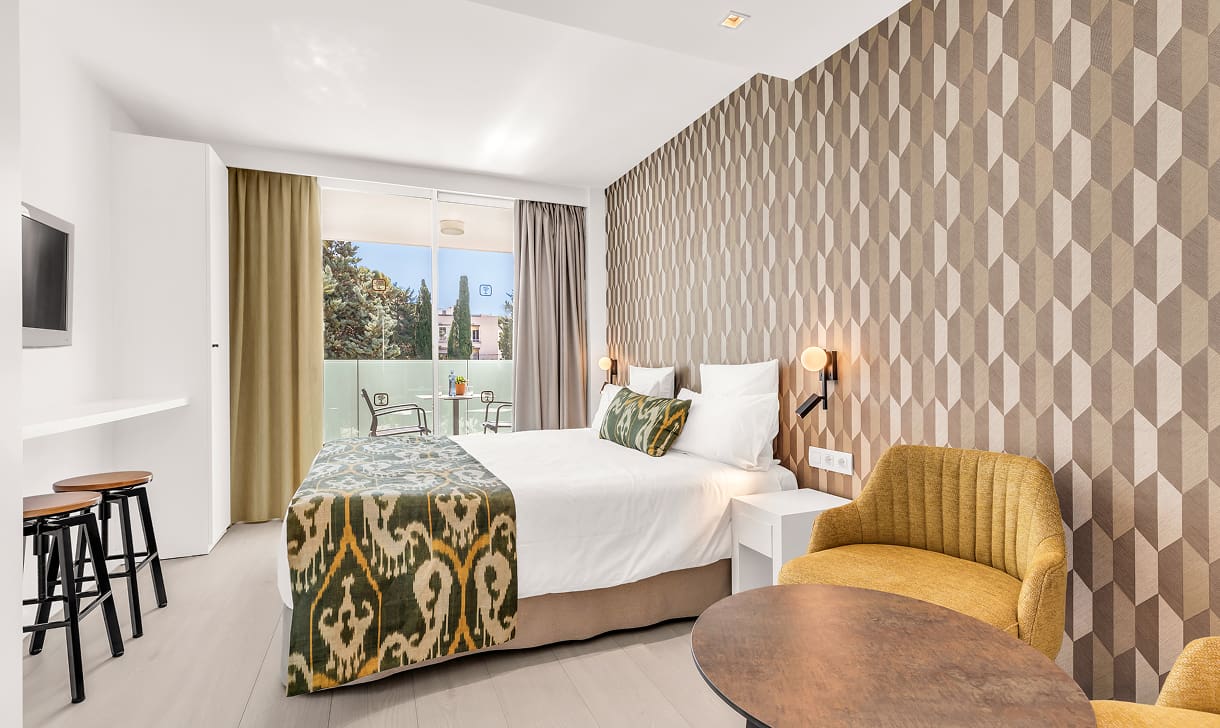 Doppelzimmer mit geometrischer Tapete, Tagesdecke aus mallorquinischem Stoff, gelbem Sessel und Terrasse