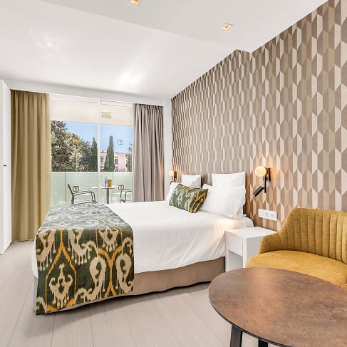 Doppelzimmer mit geometrischer Tapete, Tagesdecke aus mallorquinischem Stoff, gelbem Sessel und Terrasse