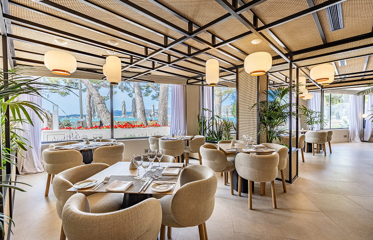 Restaurant 1929 at Hotel Illa d'Or Restaurant 1929 dining room with set tables, upholstered chairs and large windows overlooking Puerto Pollensa