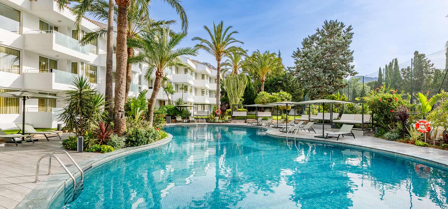 Tranquila piscina exterior rodeada de palmeras y jardín en la zona de apartamentos Illa d'Or Club