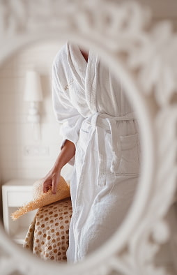 Reflection in a classic-style mirror of a guest wearing a white bathrobe in her hotel room