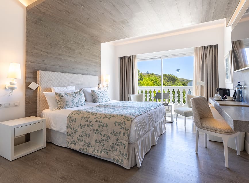 Double room with a double bed, floral bedspread, wood-panelled wall and a balcony overlooking greenery